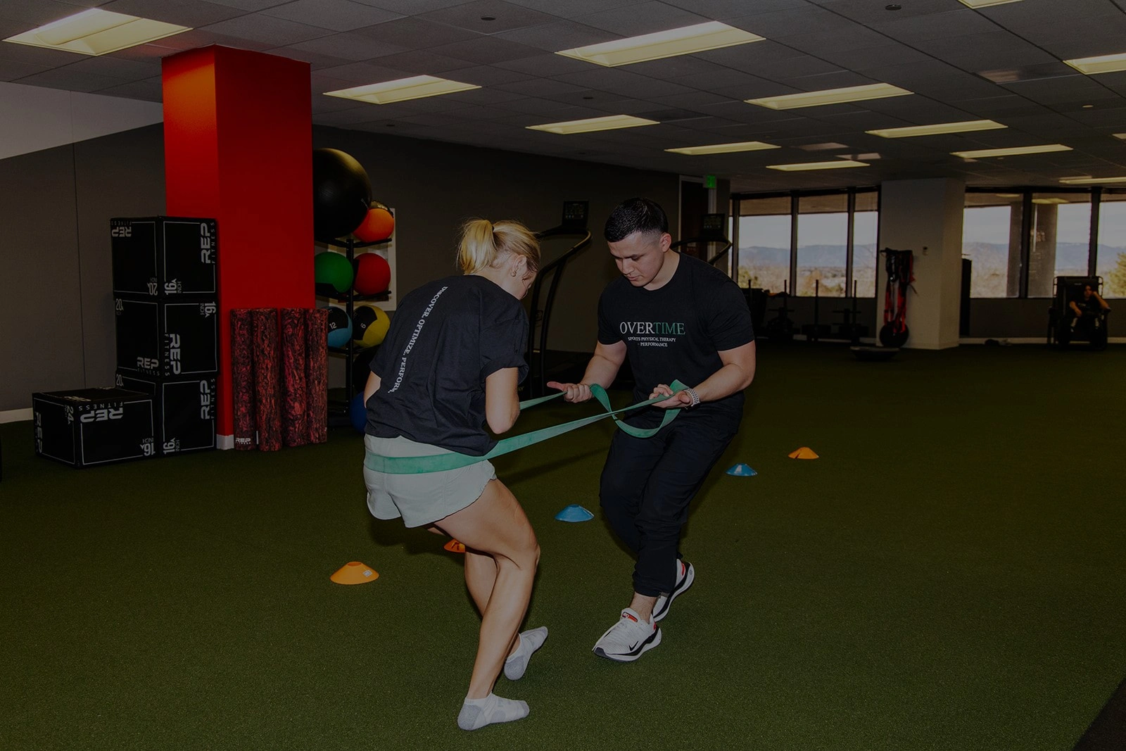 An Overtime physical therapist guiding an athlete through a resistance-band exercise.