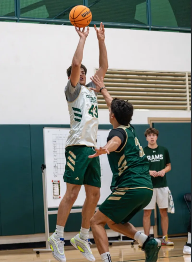 A basketball player taking a jump shot while a defender contests.