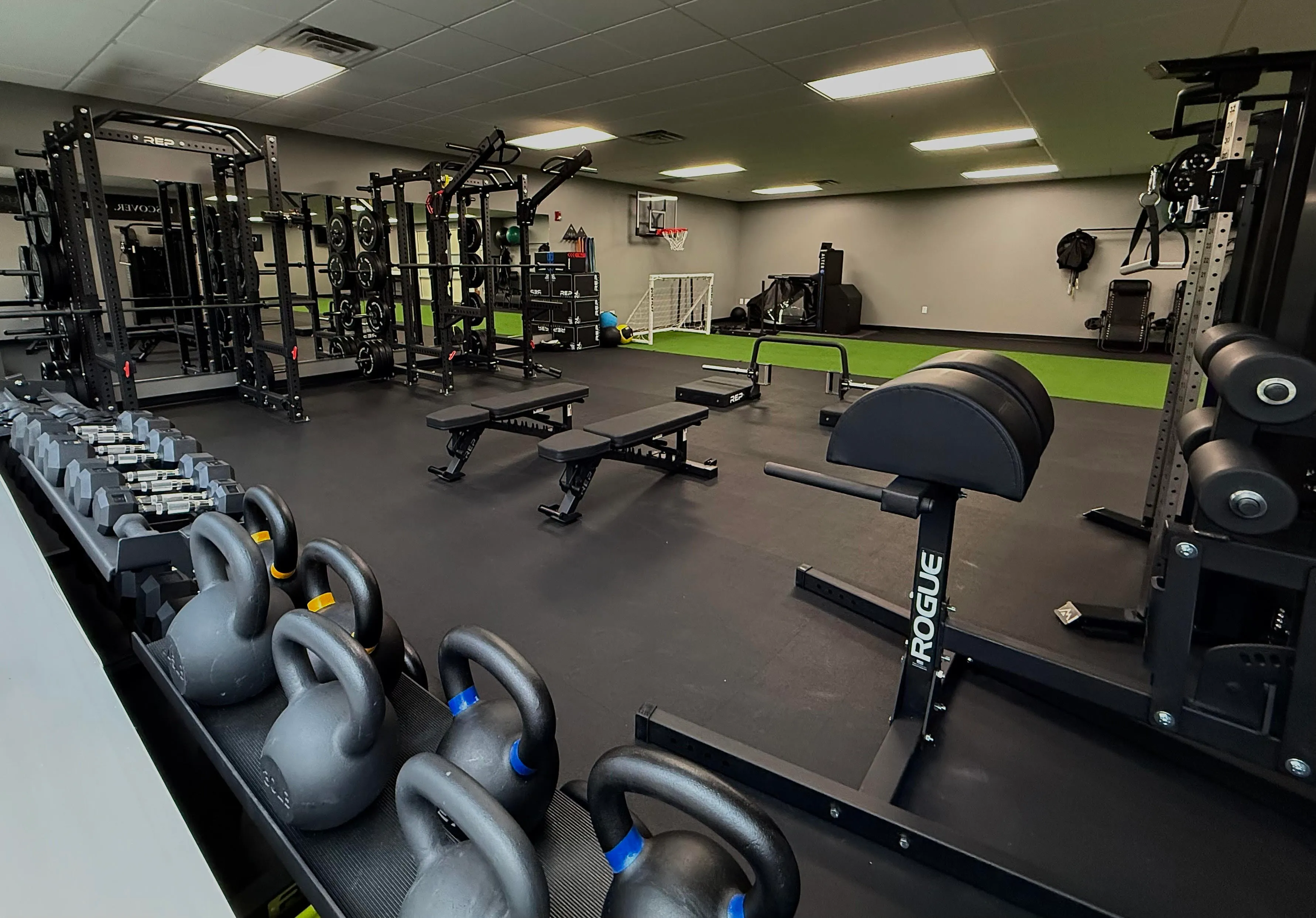 A picture of the OVERTIME Sports PT gym containing multiple types of equipement such as dumbells, benches, squat racks and a turf area.